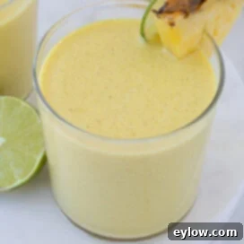A bright yellow mango pineapple smoothie in a glass with lime and fruit wedge.