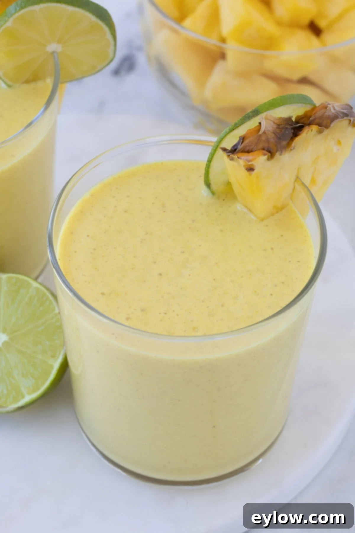 A bright yellow mango pineapple smoothie with pineapple and lime garnish.