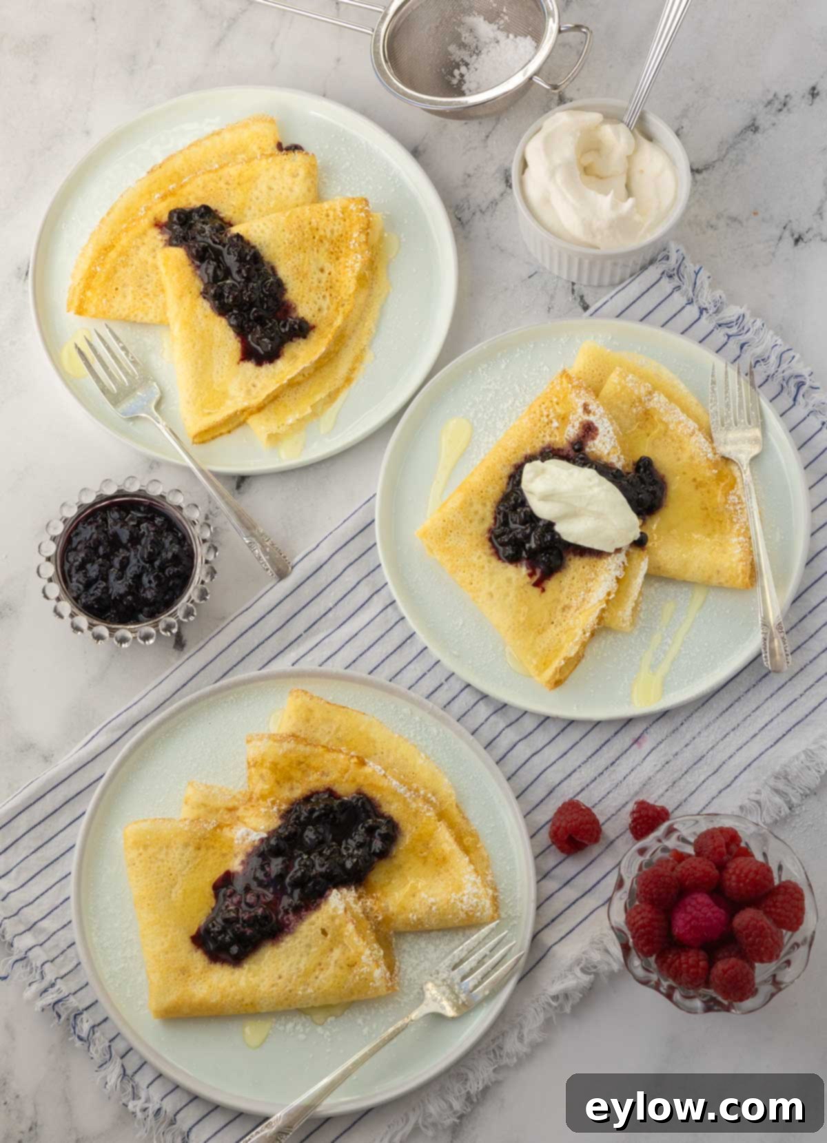 Plates of golden crepes topped with blueberries, powdered sugar, and whipped cream, invitingly presented.