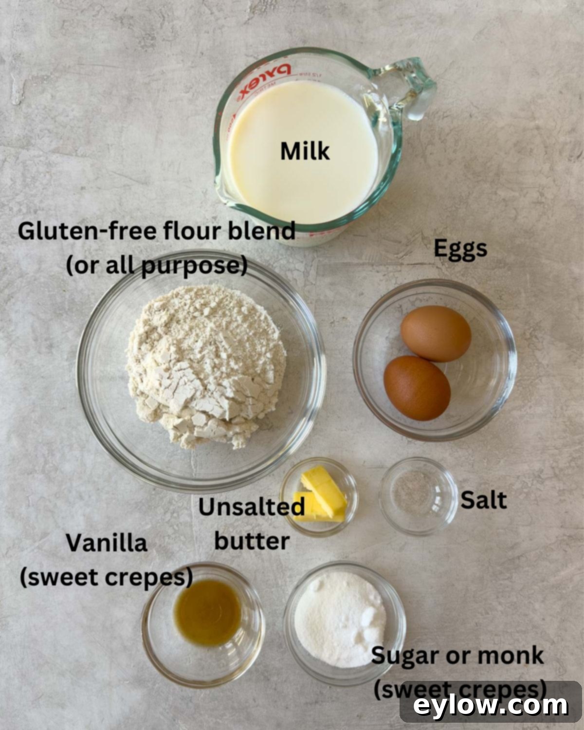Various crepe ingredients including flour, eggs, milk, and butter laid out on a kitchen counter.