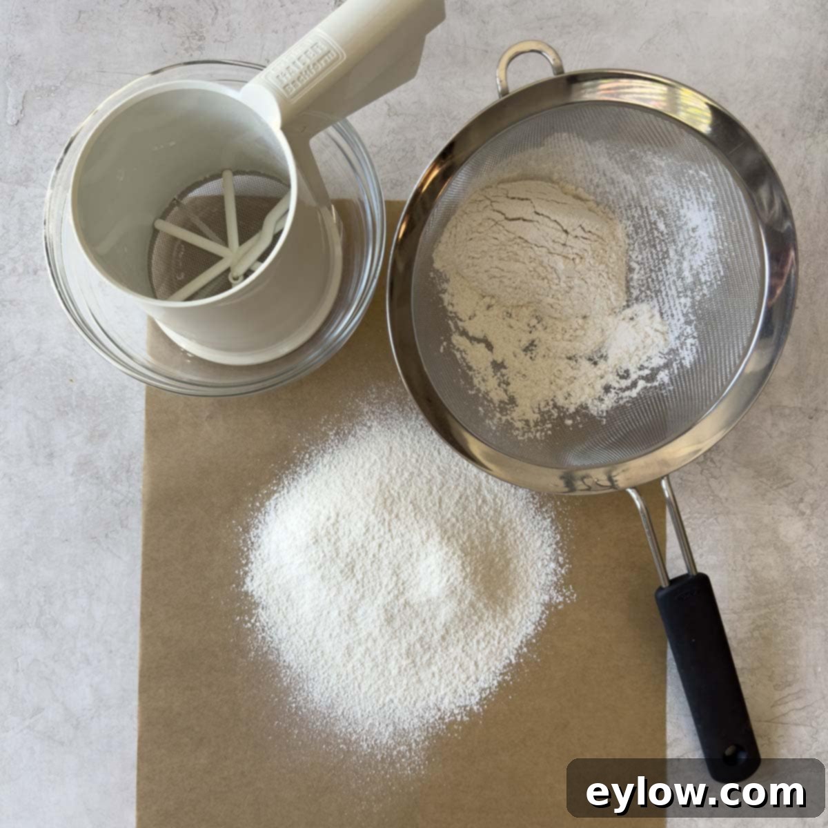 Sifted gluten-free flour on parchment paper next to a sifter and a fine sieve.