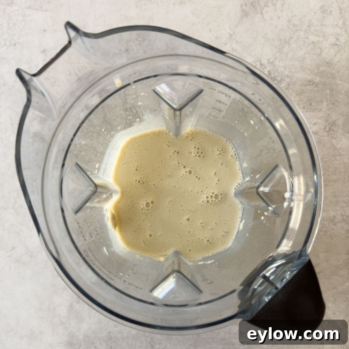 Smooth, pale yellow crepe batter inside a blender container after being blended.