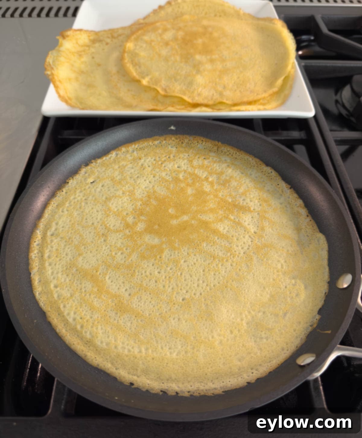 A perfectly golden-brown crepe resting in a black shallow pan after being flipped, ready to be removed.