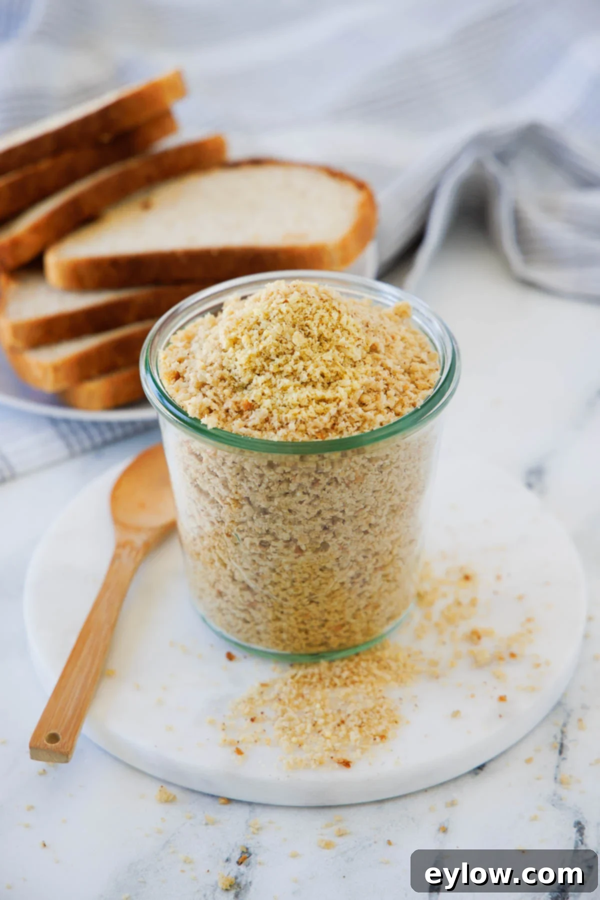 A tall jar of homemade golden breadcrumbs on a round white plate, ready for use.