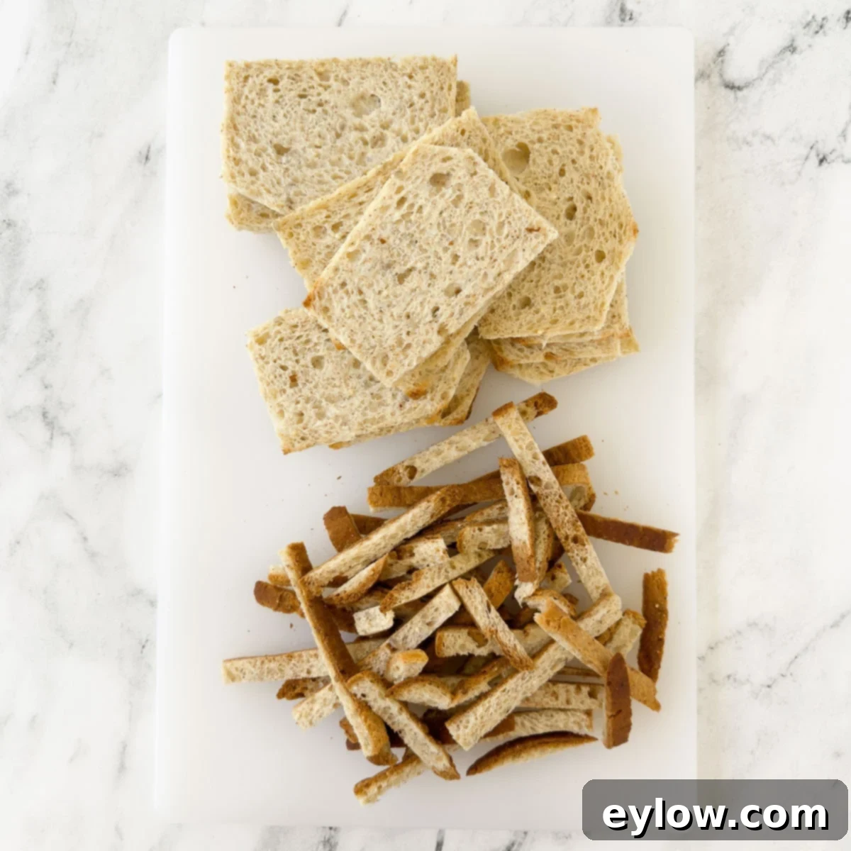 A cutting board with gluten-free bread slices, some trimmed of crusts, ready for preparation.