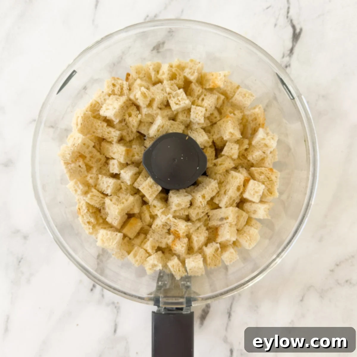 Gluten-free bread cubes placed in the workbowl of a food processor, ready for pulsing.
