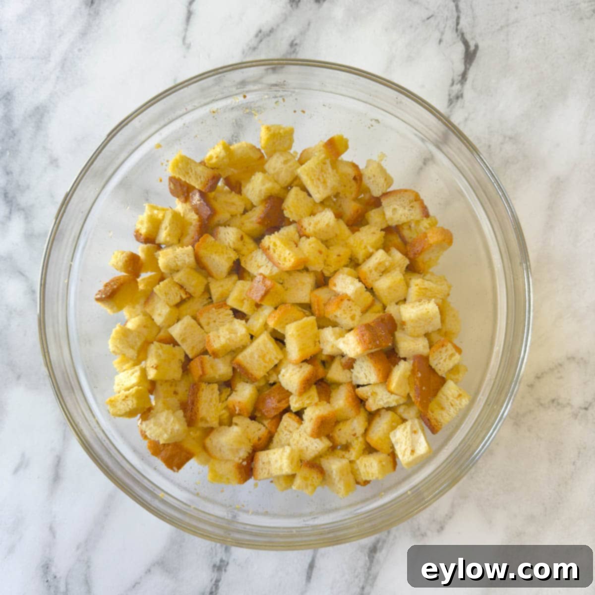 Bread cubes tossed with butter and olive oil in a glass bowl.