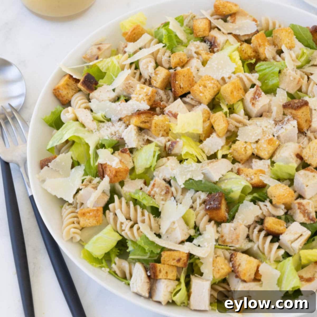 Emperor's Chicken Pasta Salad 10 A Caesar pasta salad ready to serve with salad servers and dressing in a marble counter.