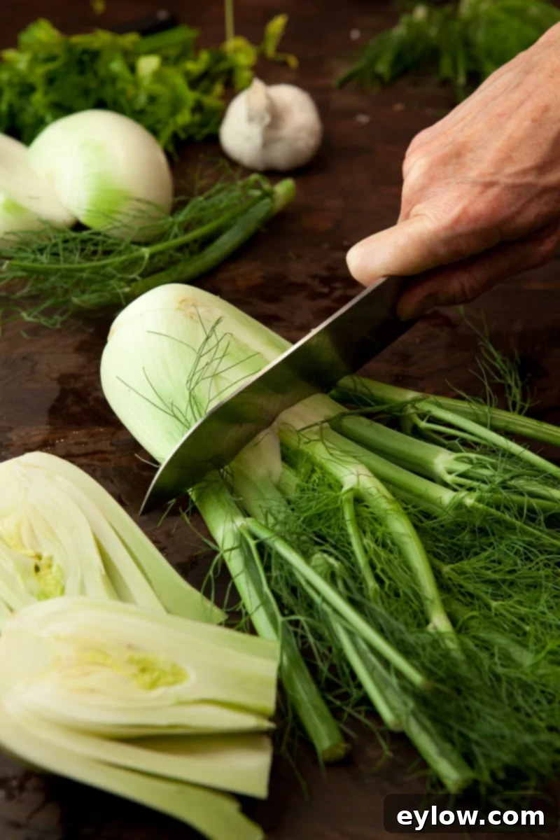 Chopping the top stalks off of a fennel bulb on a dark brown walnut cutting board.