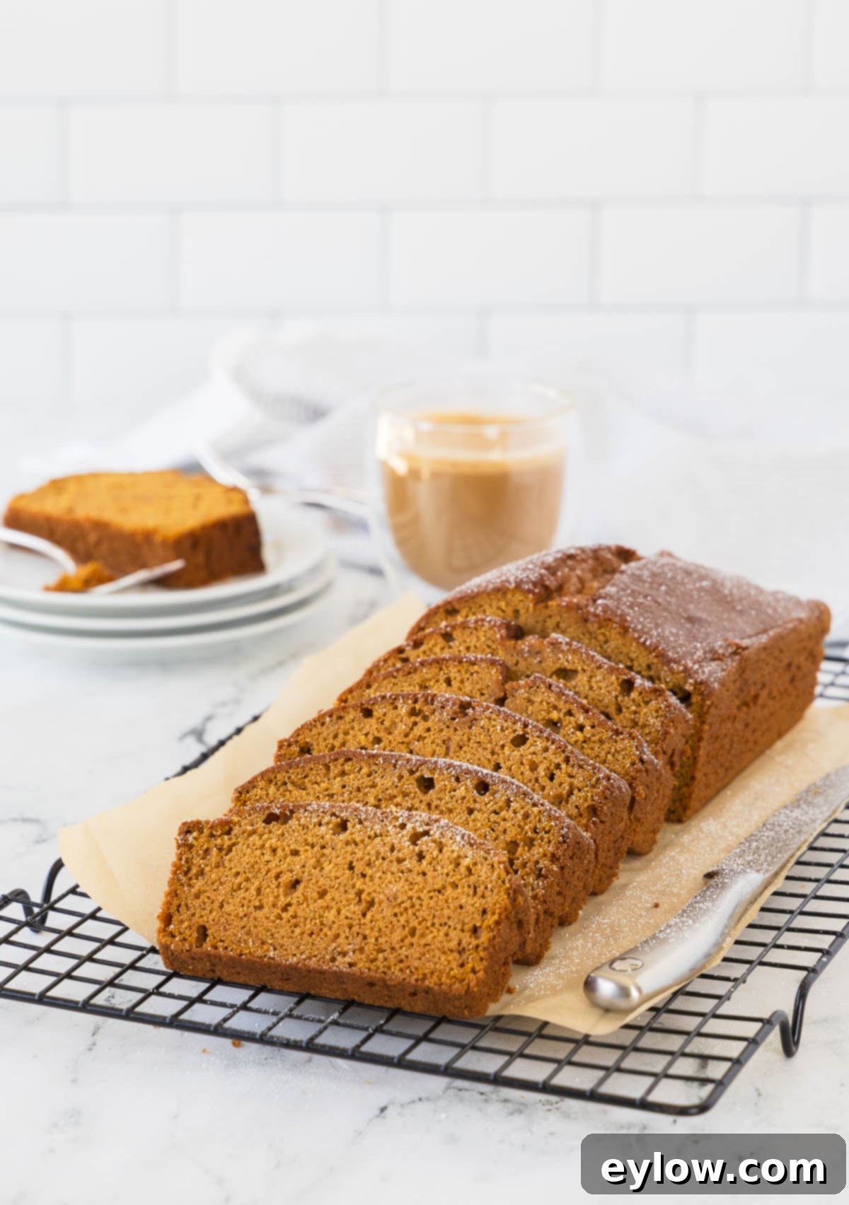 A beautifully sliced loaf of moist pumpkin bread, showcasing its tender crumb, resting on a wire cooling rack alongside a knife and a steaming cup of coffee, ready to be enjoyed.