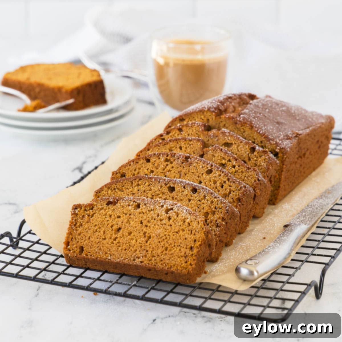A golden-brown loaf of moist pumpkin bread, expertly sliced and arranged to highlight its tender texture, poised to be savored with a cup of coffee, creating a perfect autumnal scene.
