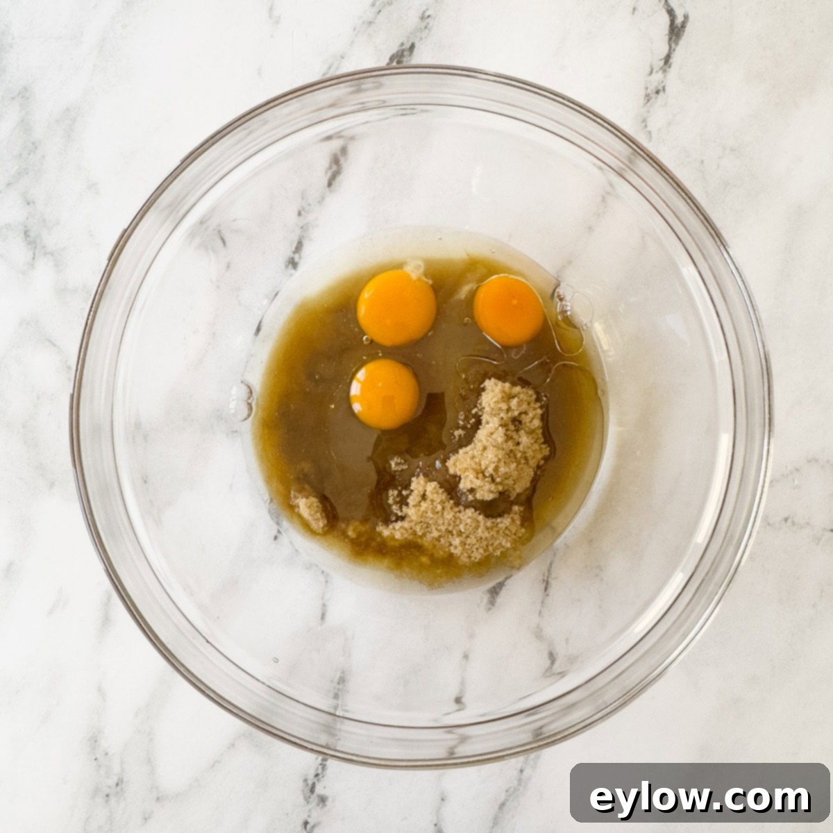 Wet ingredients for pumpkin bread—fresh eggs, healthy neutral oil, creamy pumpkin puree, light brown sugar, and aromatic vanilla extract—prepared in a separate glass bowl, poised for mixing.