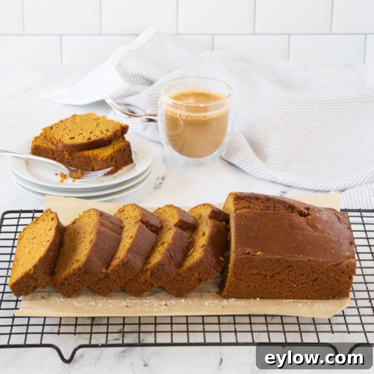A perfectly golden-brown loaf of gluten-free pumpkin bread, freshly baked and expertly sliced, resting on a sleek black wire cooling rack, emitting a comforting aroma.