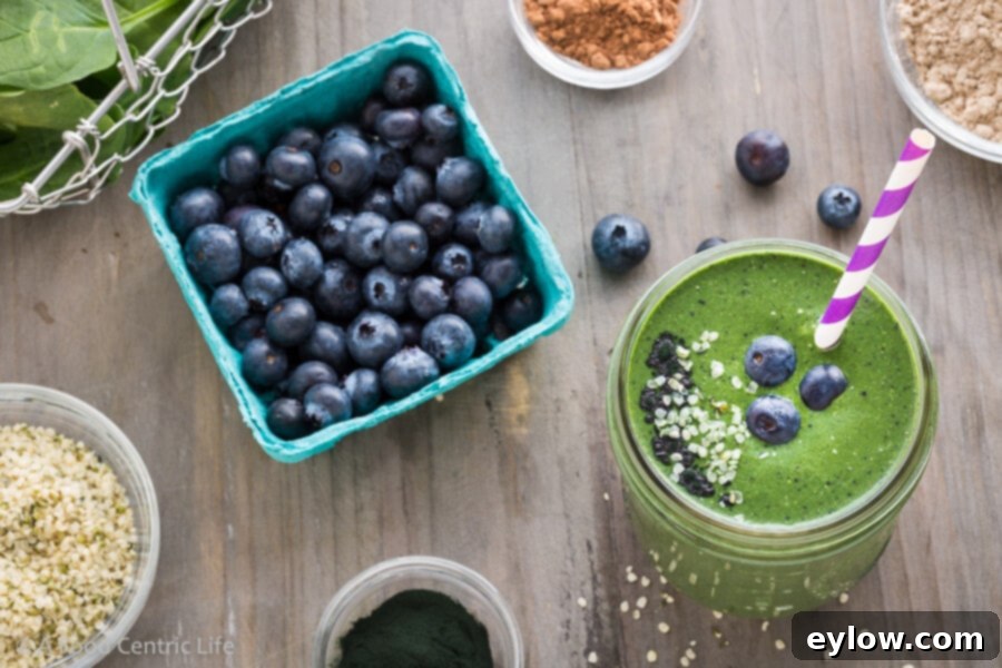 A delicious Superfood Blueberry Green Smoothie in a glass, with fresh blueberries and spinach leaves scattered around.