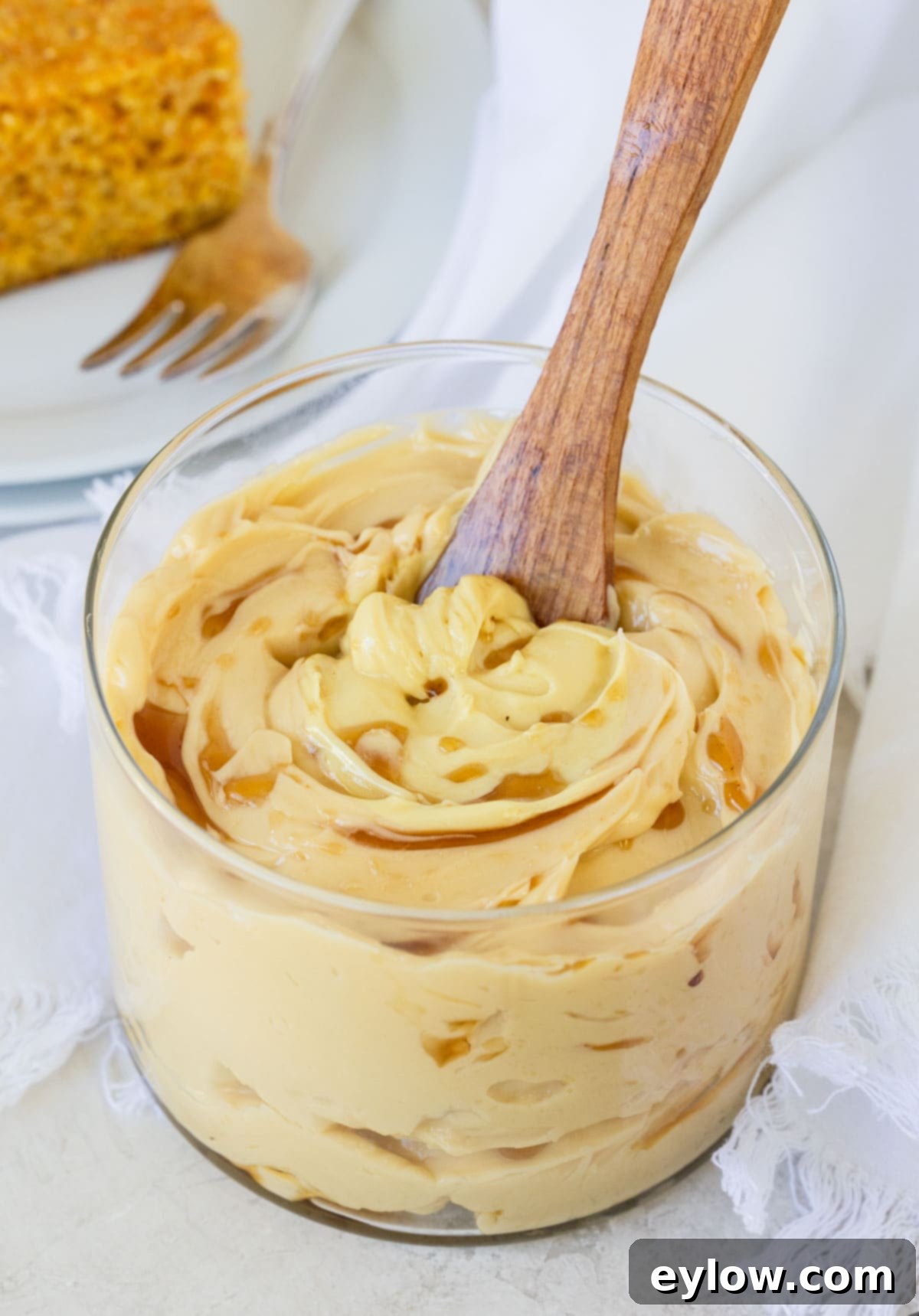 A jar of homemade maple butter with maple drizzle on top and a small wooden spreader. The butter is light brown and smooth.