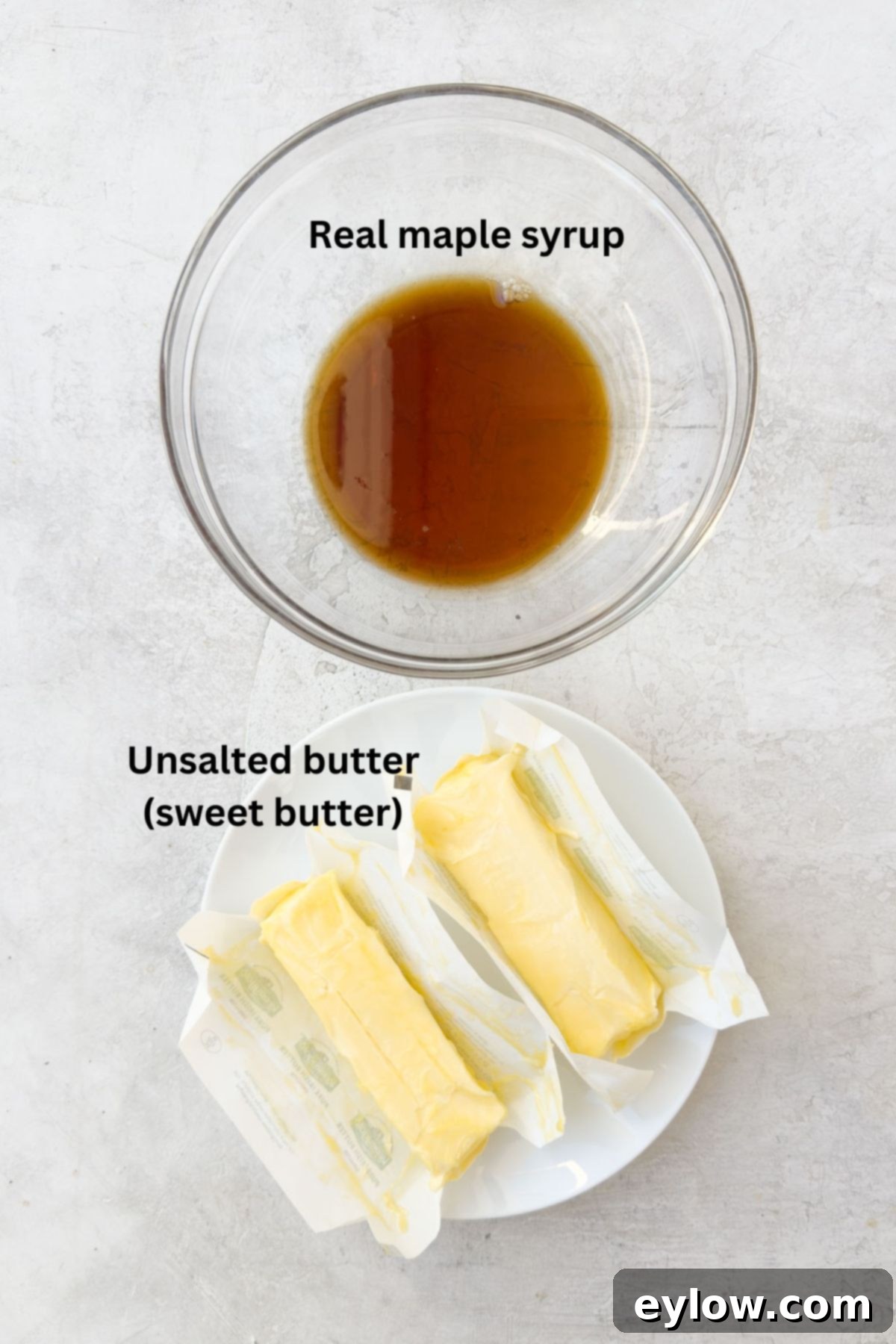 Simple ingredients for making maple butter, showing unsalted butter sticks and a bottle of maple syrup on a kitchen counter.
