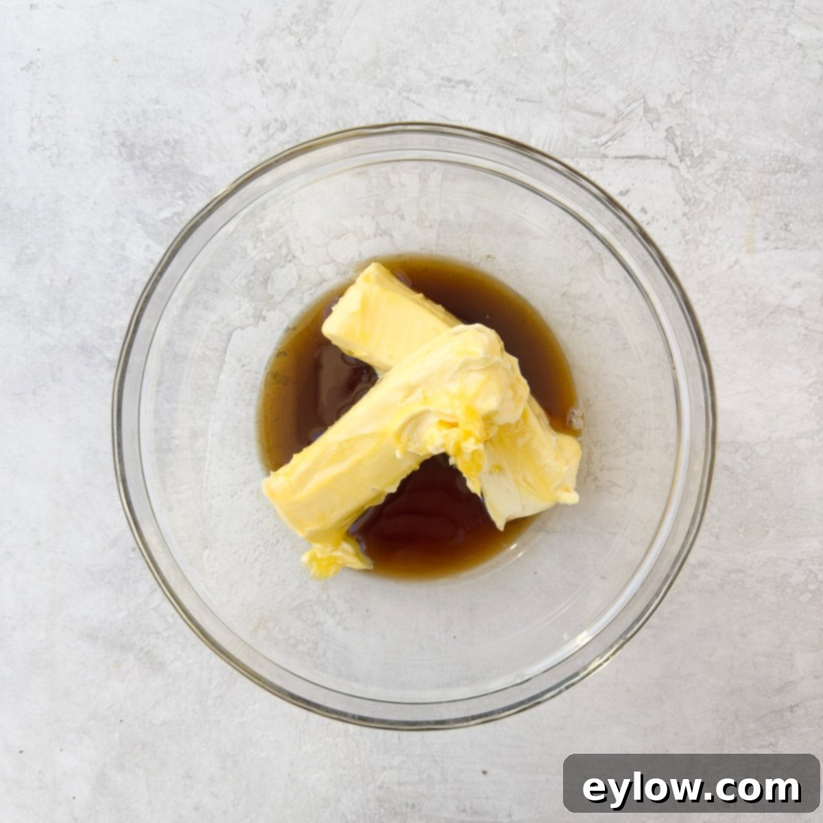 Two sticks of butter in a glass bowl with maple syrup being poured over them.