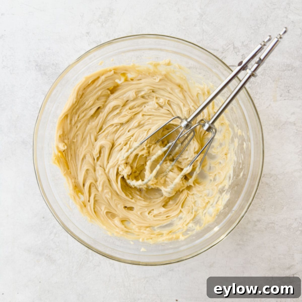 Whipped maple butter in a glass bowl with silver beaters from a hand mixer. The butter is light and airy.