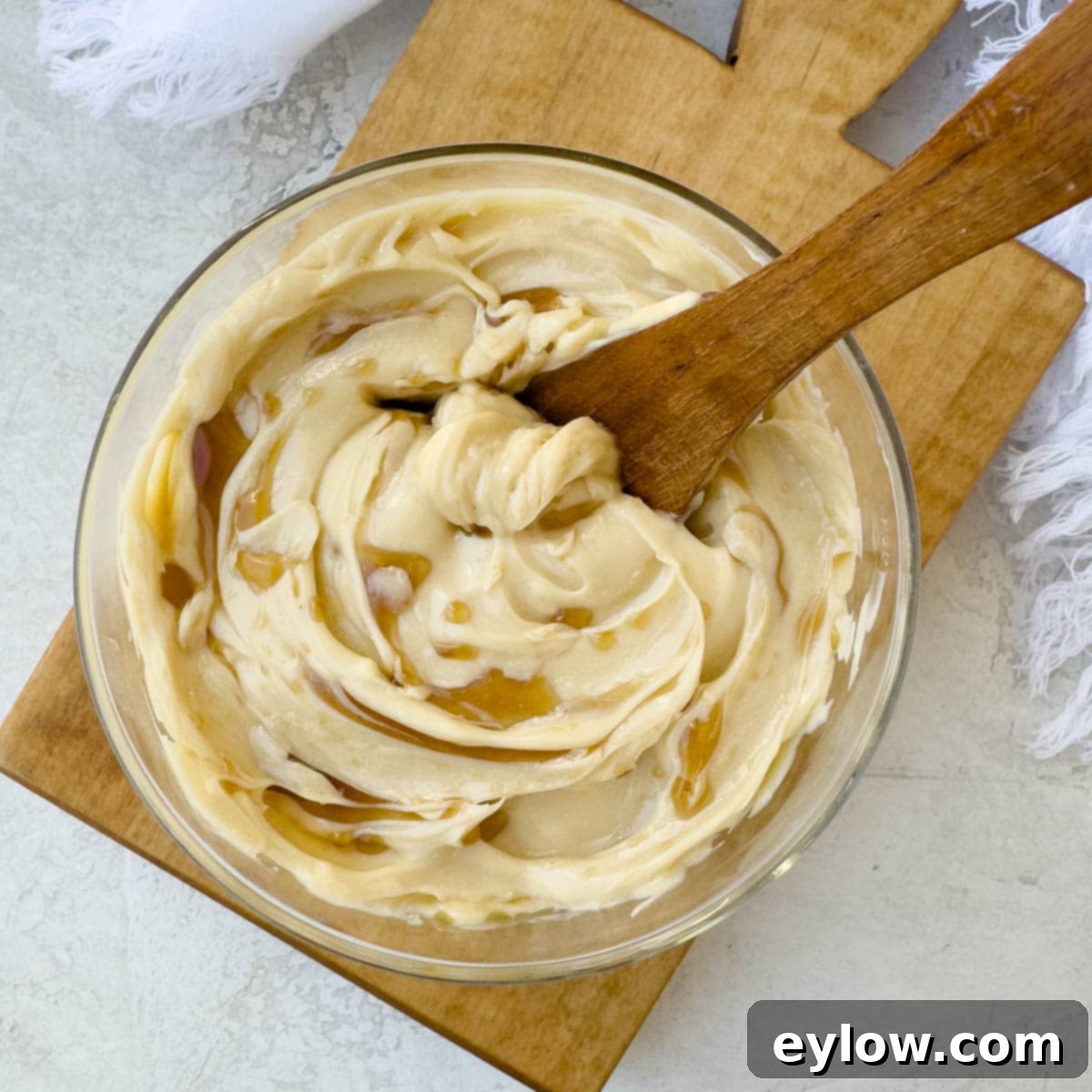 A bowl of finished maple butter with a swirl on top, a maple drizzle, and a wooden spreader resting in it. The butter looks rich and creamy.