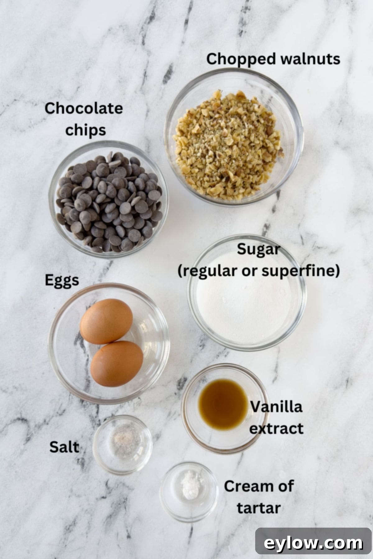 A collection of ingredients for chocolate chip meringue cookies, neatly arranged in small prep bowls on a kitchen counter.