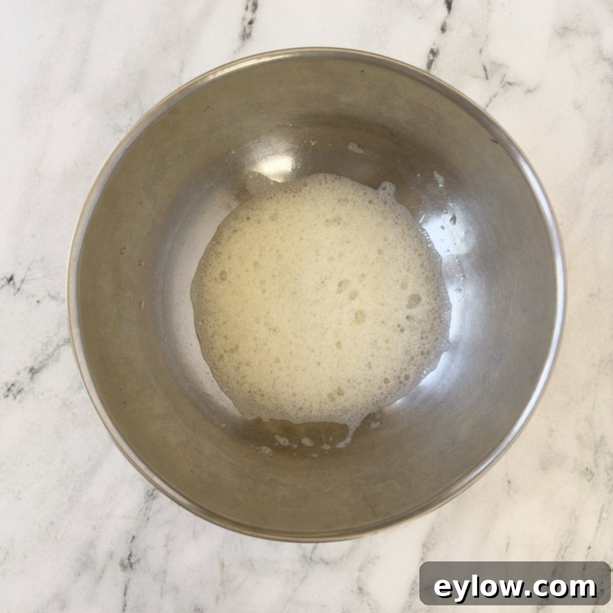 Beaten egg white at the light foamy stage in a stainless steel bowl, indicating the beginning of meringue formation.