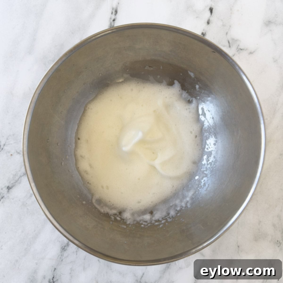 Meringue whipped to the soft peak stage in a silver mixing bowl, showing gentle peaks that collapse slightly.
