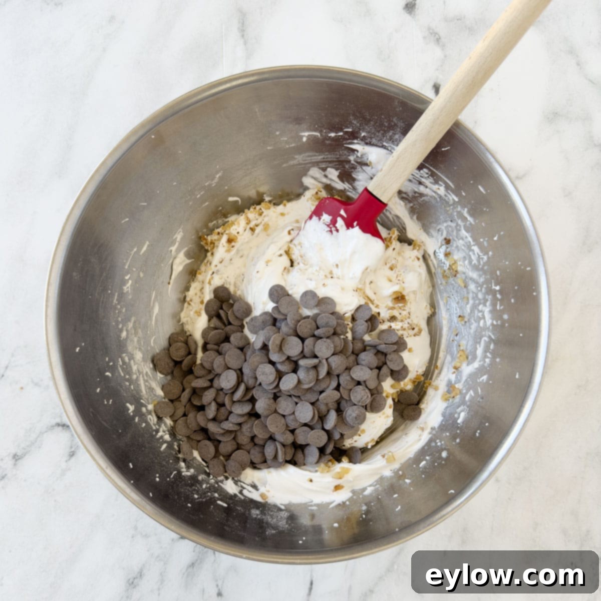 A rubber spatula carefully folding chocolate chips into the delicate meringue batter for cookies, preserving the airiness.