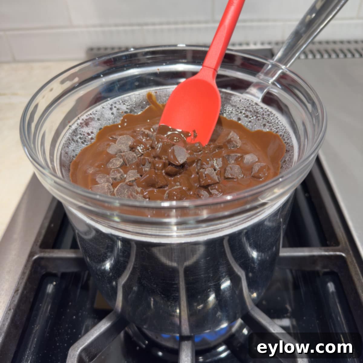 Close-up of chocolate melting gently in a double boiler set on a stovetop, with steam visible.
