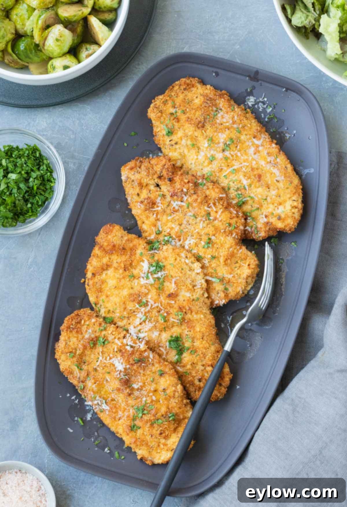 Four golden crisp air fryer chicken cutlets with a sprinkle of parmesan and parsley, gray platter.
