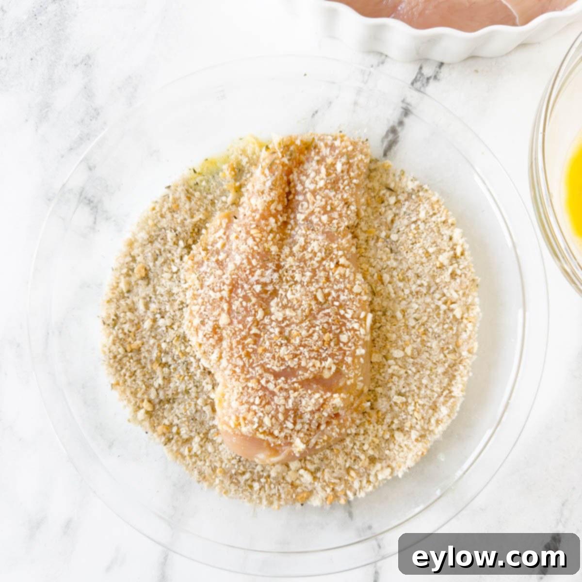 A panko coated chicken breast in a pie plate being breaded.