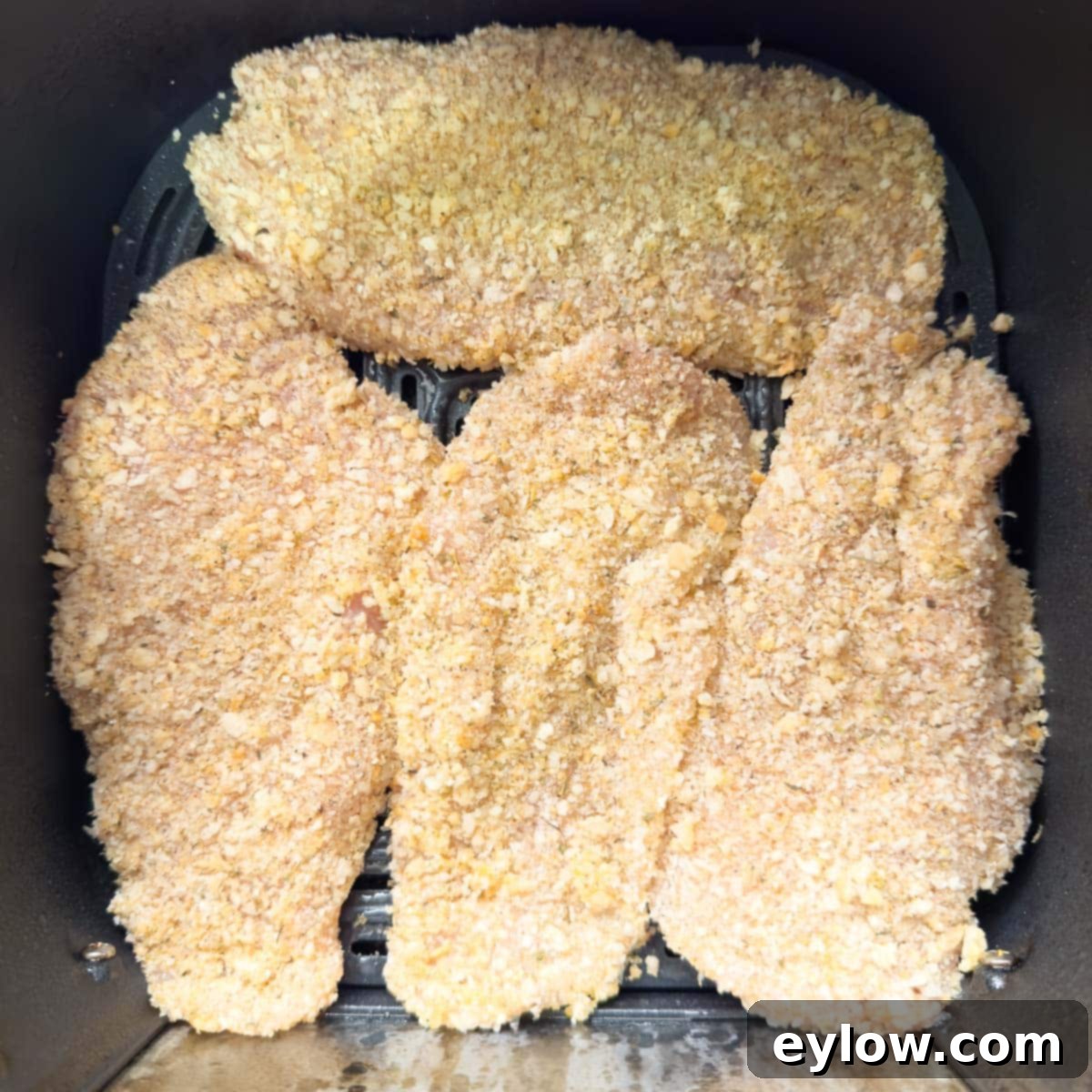 Breaded chicken cutlets in an air fryer basket ready for cooking.