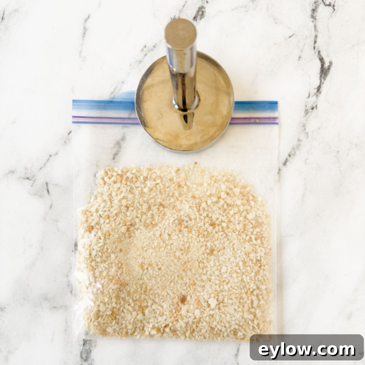 Crushed breadcrumbs in a plastic bag with a meat pounder beside on counter.