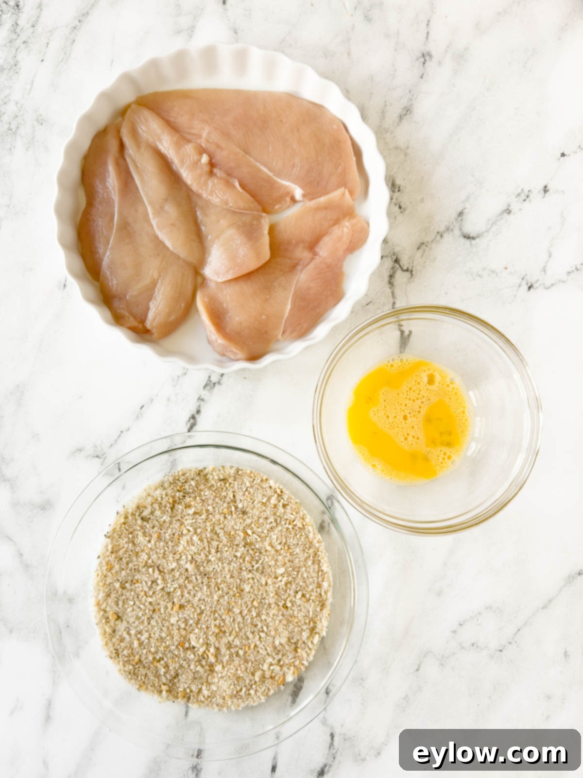 Chicken cutlets breading station with egg and seasoned coating.