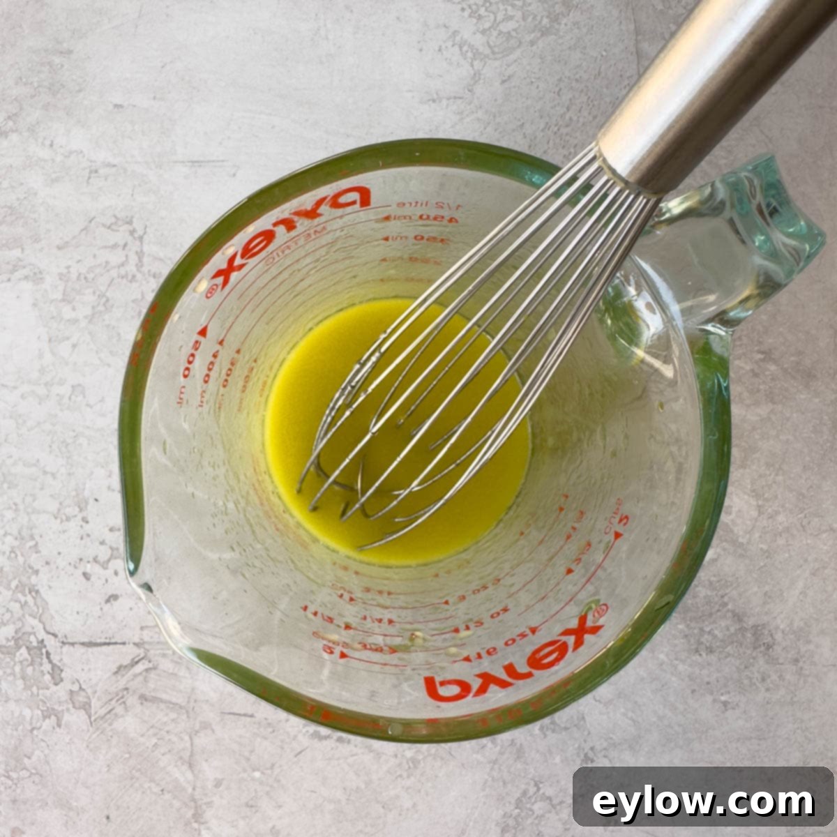 Whisking golden colored vinaigrette in a glass measuring cup.