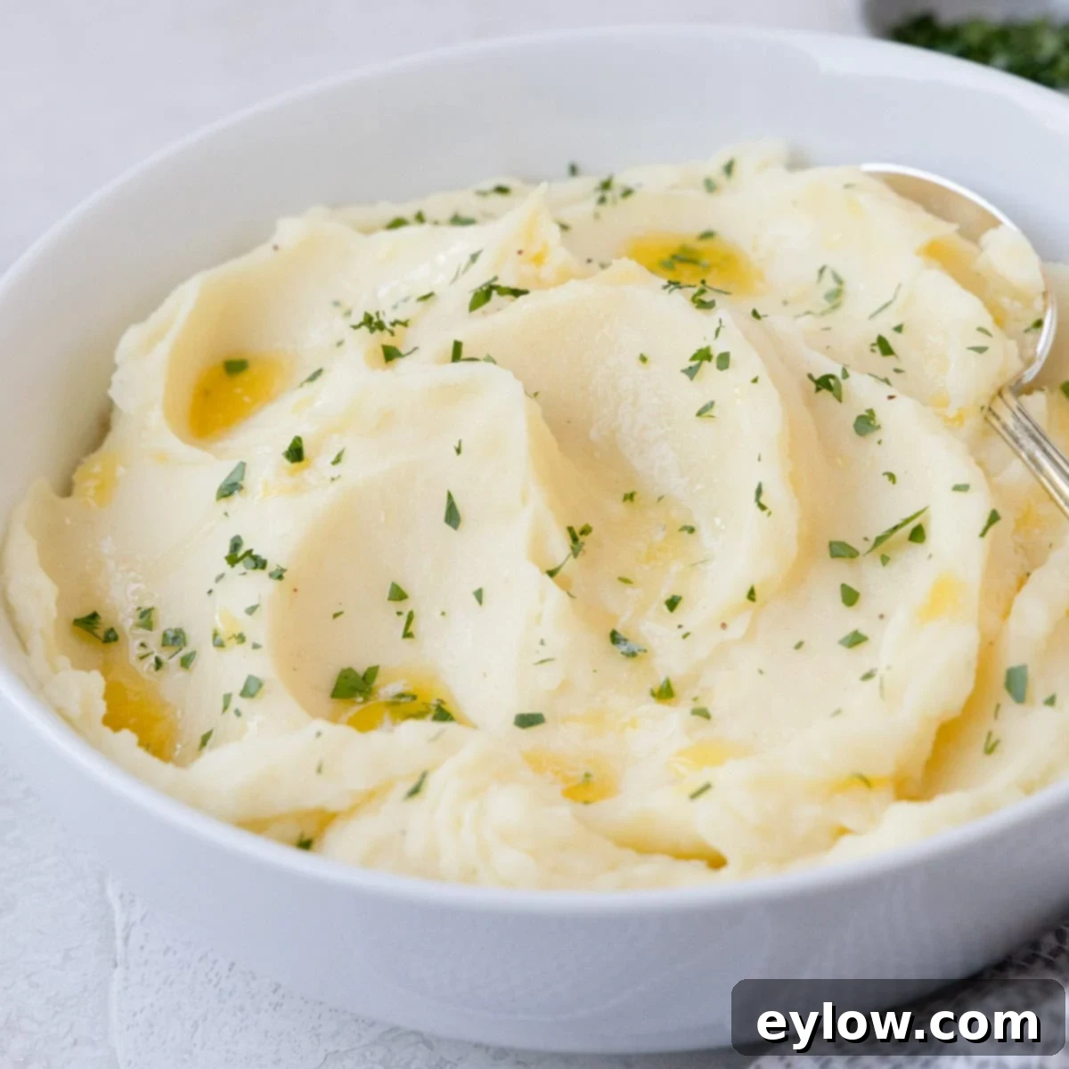 Creamy mashed potaotes with fresh chopped herbs on top and a serving spoon.
