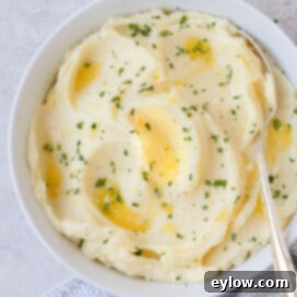 A bowl of creamy mashed potatoes with melted butter and fresh chopped parsley with a silver serving spoon.