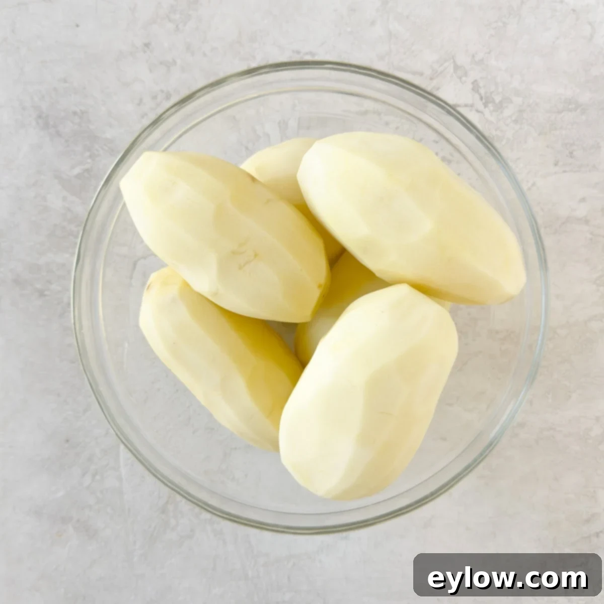 A glass bowl of clean peeled russet potatoes ready to cook.