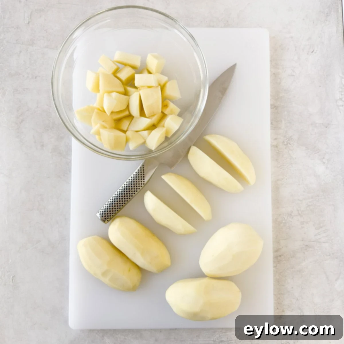 Chopped potatoes on a white cutting board with a chefs knife.