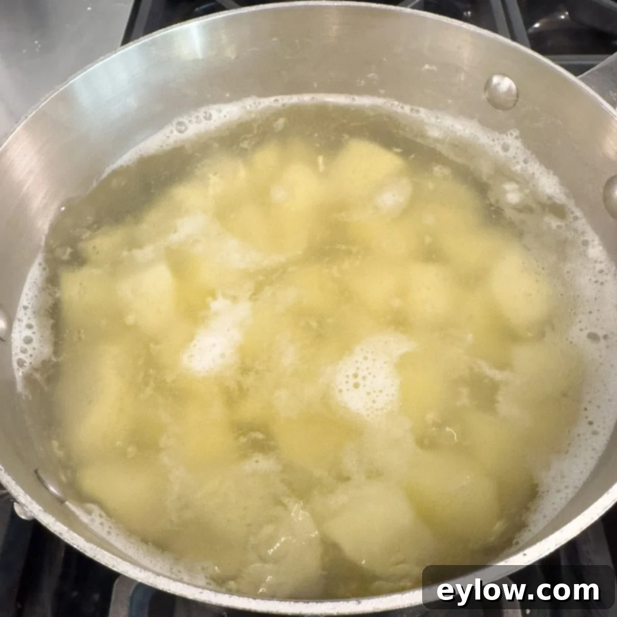 Potatoes simmering in a pot of water with small bubbles on top.