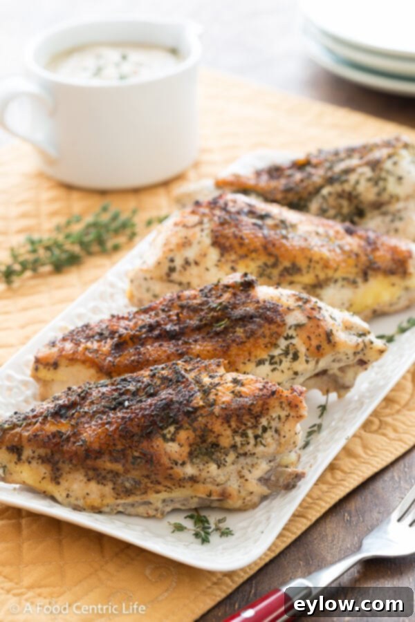 Braised chicken breasts on a platter with gravy boat of cashew sauce. 