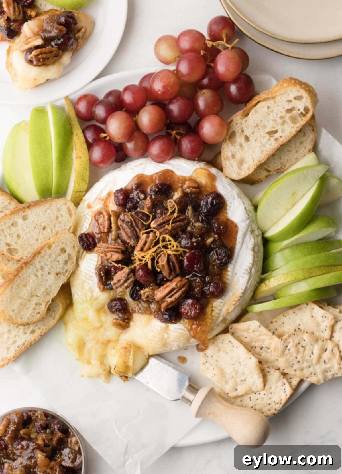 Effortless Baked Brie with Jam 2 A platter of bake brie cheese with fig jam, cranberries, pecans, and bread with apple slices.