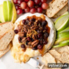 Effortless Baked Brie with Jam 9 A round wheel of baked brie cheese with a fruit and nut topping, with apples, pears, and crostini.