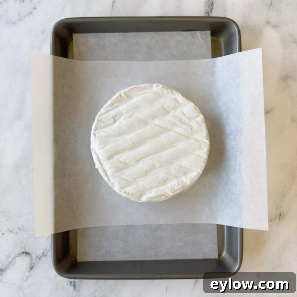 Effortless Baked Brie with Jam 4 A round wheel of brie cheese on parchment paper on a baking sheet.