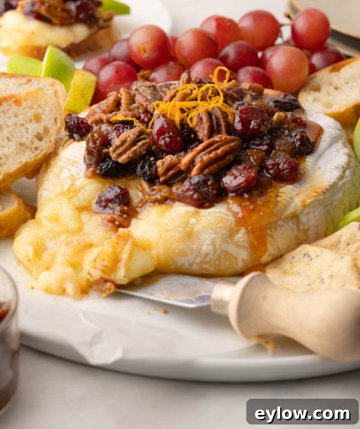 Effortless Baked Brie with Jam 8 Warm brie cheese oozing out of the wheel on a platter topped with fruit and nut sauce.