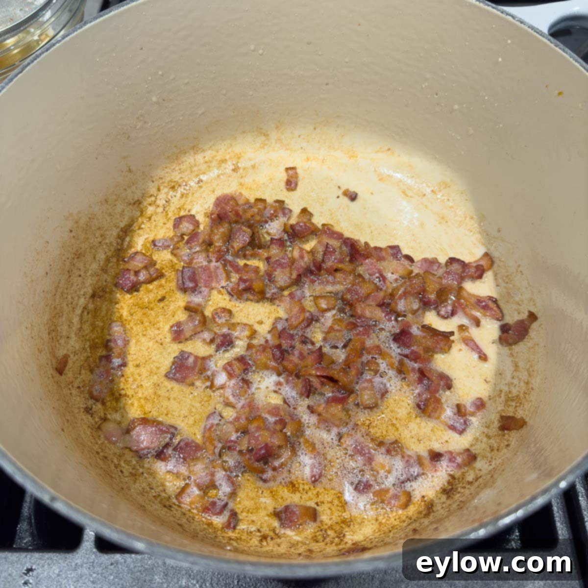 Golden, crispy cooked bacon strips resting in a heavy pot, with rendered fat visible.