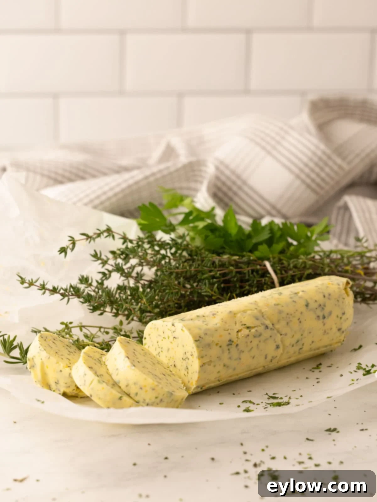 A yellow log of compound butter flecked with green herbs rolled in parchment paper.