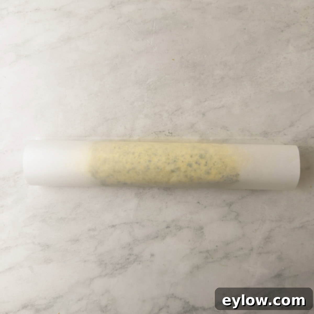 A log of herbed butter in wax paper with open ends, not twisted yet.