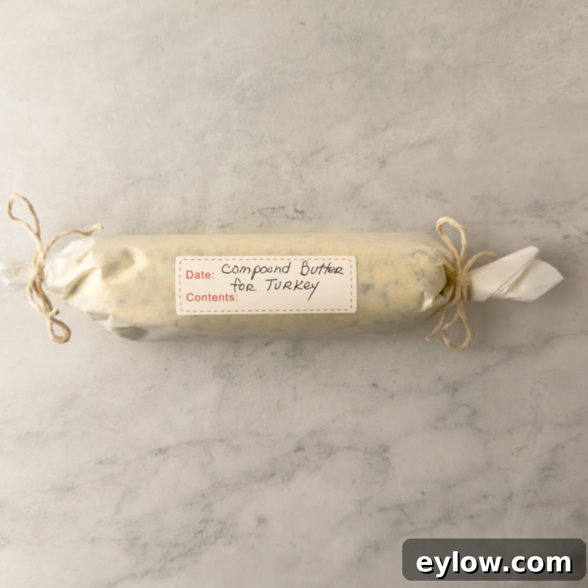 A finished log of herbed butter with ends twisted to secure and seal, with a label.