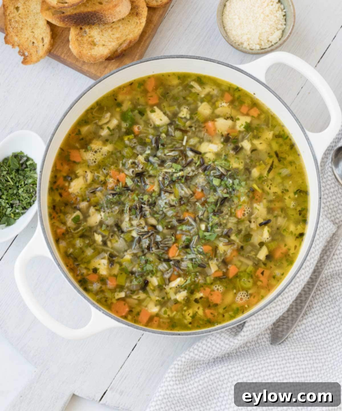 A white pot filled with hearty turkey and wild rice soup, garnished with fresh herbs and a side of golden garlic toast.