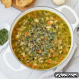A white pot of turkey and wild rice soup on a gray wooden board with herbs and parmesan cheese on the side.